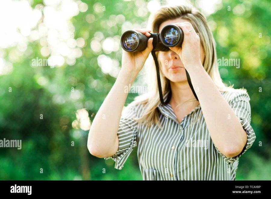 a-woman-looks-through-binoculars-outdoor-in-forest-before-sunset-TCAXBP.jpg