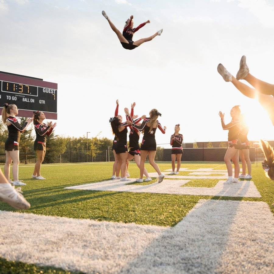 teenage-girl-high-school-cheerleading-team-performing-double-nine-jump-on-sunny-football-field...jpg